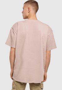 Lyserød oversized t-shirt; bomuldsmateriale; rund hals; korte ærmer; flade sømme; afslappet pasform; bagvisning viser ingen synlige mønstre eller grafikker.