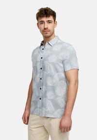 Camisa de botones de manga corta en azul claro con un patrón de hojas tropicales en blanco. Presenta un cuello extendido y botones oscuros, confeccionada en una tela ligera.