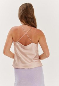 Saténová košilka v světle růžové barvě s volným siluetou, má křížové ramínka a hladký povrch, doplněná levandulovou sukní.