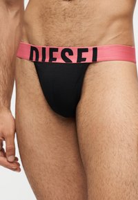 Άνω κορμός άνδρα που φοράει μαύρο jockstrap εσώρουχο με φαρδιά ροζ ζώνη μέσης και μεγάλο μαύρο λογότυπο "DIESEL".