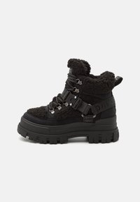 Black ankle boots with a textured fur-like upper, sturdy rubber sole, metal eyelets, and adjustable buckle straps. Bold design with a cushioned collar.