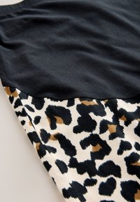 Tissu noir drapé sur un tissu à imprimé léopard avec des taches irrégulières noires, brunes et blanches.