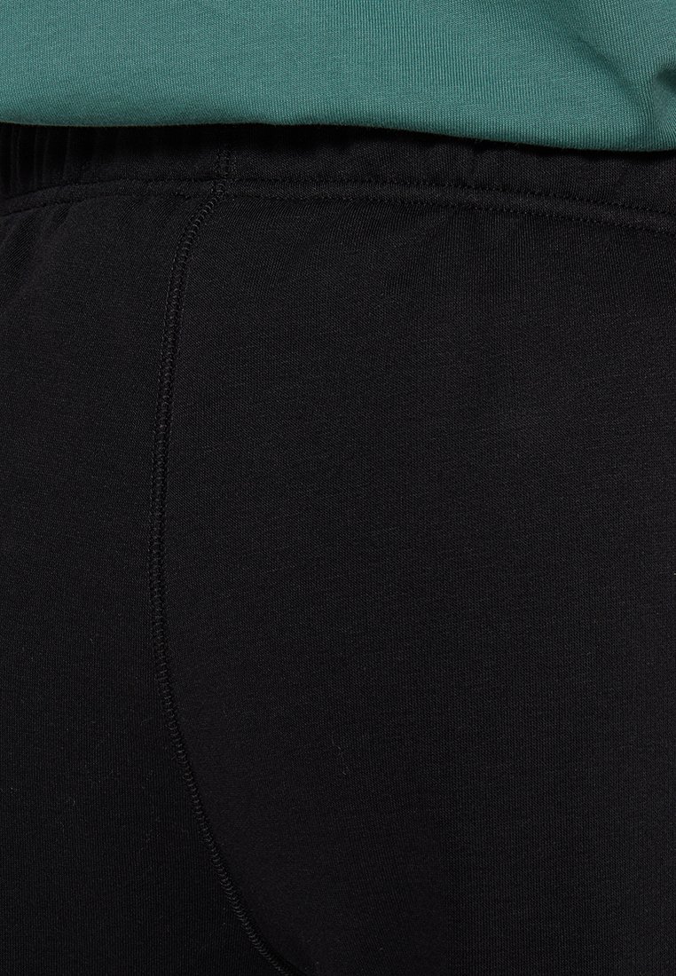Pantaloni in tessuto elasticizzato nero con cintura elasticizzata. Texture liscia, cuciture minimali e design aderente. Nessun motivo o accento evidente.