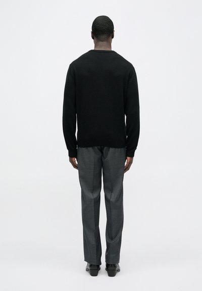 Černý pletený svetr s žebrovaným výstřihem, spárovaný se šedými na míru ušitými kalhotami. Výrazné jsou čisté linie, jednobarevné odstíny a strukturovaný střih.