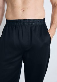 Black, lightweight trousers with an elastic waistband and side pockets. Smooth texture, tailored fit, and no visible patterns or hardware.