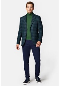 Męska marynarka w zielono-granatową kratę, zestawiona z zielonym golfem. Granatowe spodnie i granatowe sneakersy dopełniają całość.