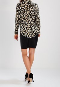 Blusa de leopardo en tejido ligero, combinada con una falda negra. Presenta mangas largas y un dobladillo curvado. Unos zapatos de tacón negro completan el conjunto.