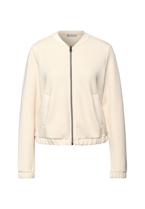 Giacca zip con colletto rotondo di colore crema chiaro, con due tasche laterali, polsini a coste e vita aderente. Tessuto liscio e morbido con un leggero lucido.