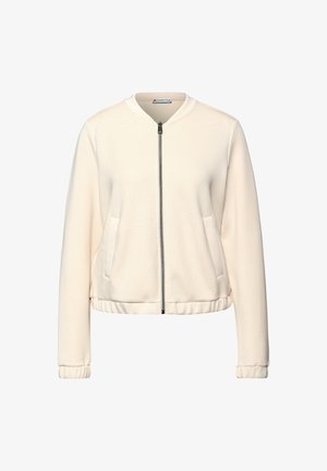 Giacca zip con colletto rotondo di colore crema chiaro, con due tasche laterali, polsini a coste e vita aderente. Tessuto liscio e morbido con un leggero lucido.
