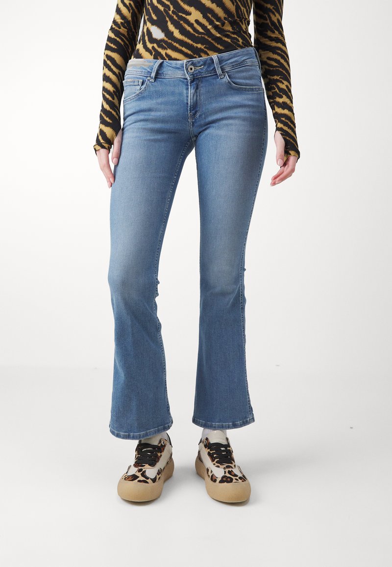 Jeans flare bleu clair en denim avec une légère décoloration. Associés à des baskets beiges et imprimé animal. Haut à motifs avec des manches longues.