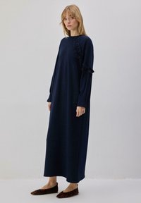 Robe à manches longues bleu marine en tissu doux. Présente des détails à volants sur un côté. Associée à des ballerines imprimé léopard marron.