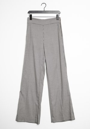 Pantalones de pierna ancha pequeños a cuadros en blanco y negro colgados en una percha de plástico negra con cremallera lateral.