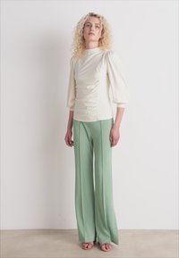 Cream puff-sleeve top with ruching detail paired with high-waisted, wide-leg mint green trousers. Worn with light brown open-toe sandals.