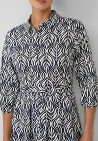 Kragenkleid in Marineblau mit einem cremefarbenen Blättermuster, ausgestattet mit Dreiviertelärmeln und einem gebundenen Taillenzug für eine figurbetonte Passform.