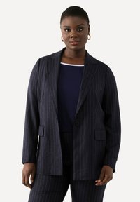 Námořnický blazer s jemným proužkem, s jedním knoflíkem, klopami a dvěma předními kapsami. Texturovaná látka dodává hloubku. Spárováno s námořnickým topem.