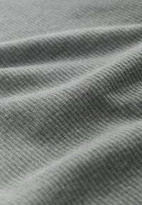 Hellgrauer Stoff mit gerippter Textur, der feine, parallele Linien in einem weichen, dehnbaren Material zeigt. Leicht zerknittertes Aussehen.