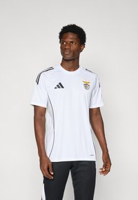 Fehér sportpóló fekete csíkokkal, a mellrészen a Benfica logójával és három csillaggal. Lélegző anyagból készült.