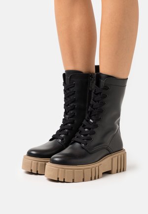 Black leather ankle boots with thick beige platform sole, featuring lace-up front and side zipper. Smooth finish, rounded toe design.