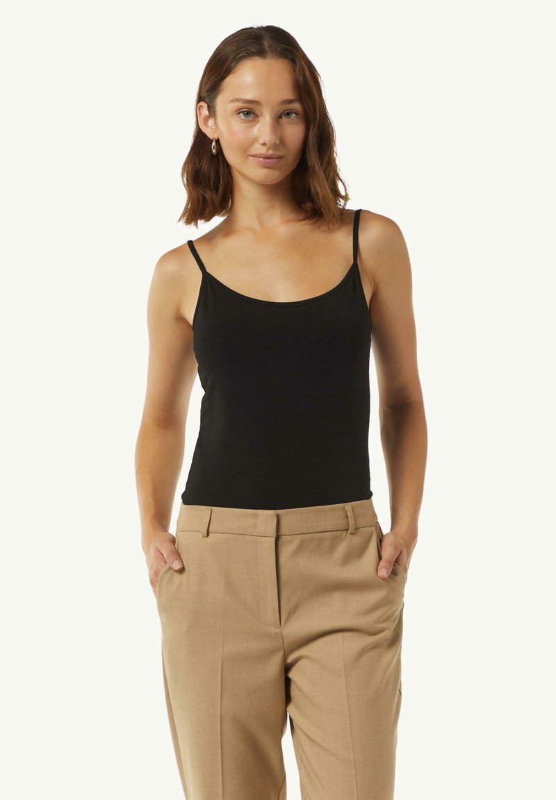 Body nera senza maniche con una texture liscia e scollatura rotonda, abbinato a pantaloni beige a vita alta con tasche laterali.