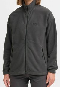 Grå fleecetrøje med høj hals, lynlås foran og sidelommer. Har et diskret logo på brystet og blødt, tekstureret materiale.