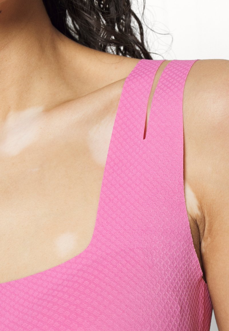 Roze gestructureerde zwemkleding met een vierkante halslijn en smalle uitsparingsbanden, die een glad oppervlak en contrasterende huidskleur laat zien.