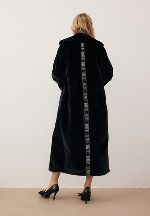 Zwarte nepbontjas met een lange silhouette, voorzien van een contrasterende verticale logo-stripe langs de achterkant en brede, zachte revers.