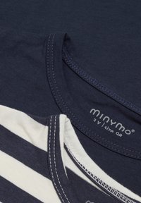 Gros plan de deux t-shirts, un uni bleu marine et un à rayures bleu marine et blanc, montrant les encolures et les détails des coutures.