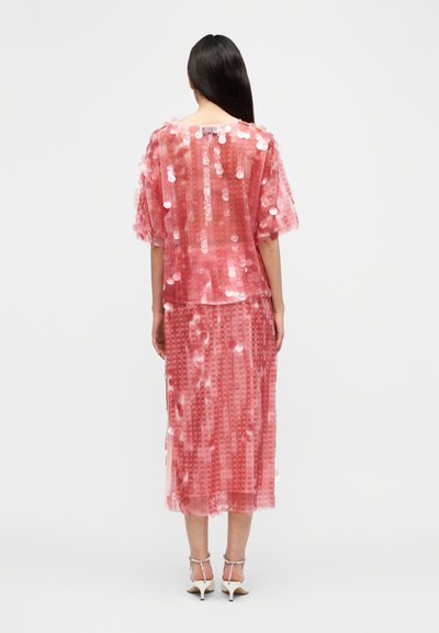 Ροζ διάφανο φόρεμα με παγιέτες, κοντά φουσκωτά μανίκια και φούστα μεσαίου μήκους με υφή και παραλλαγές σχεδίων. Συνδυασμένο με λευκά τακούνια.