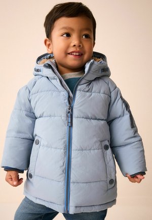 Kleines Kind lächelt und trägt eine hellblaue Steppjacke mit Kapuze und Vorderentaschen.