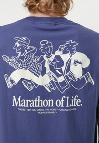 Camiseta de manga corta en azul marino con diseño gráfico blanco de tres figuras y el texto "Maratón de la Vida" debajo. Material de algodón suave.