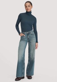 Dunkelblause Rollkragenoberteil kombiniert mit hellblauen, weit geschnittenen Jeans mit hoher Taille, ausgewaschenem Finish und Taschendetails. Schwarze Schuhe inklusive.