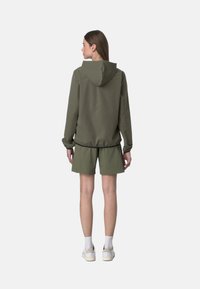 Giacca verde con cappuccio e polsini elasticizzati, abbinata a pantaloni corti coordinati. Presenta una texture liscia e una vestibilità comoda.