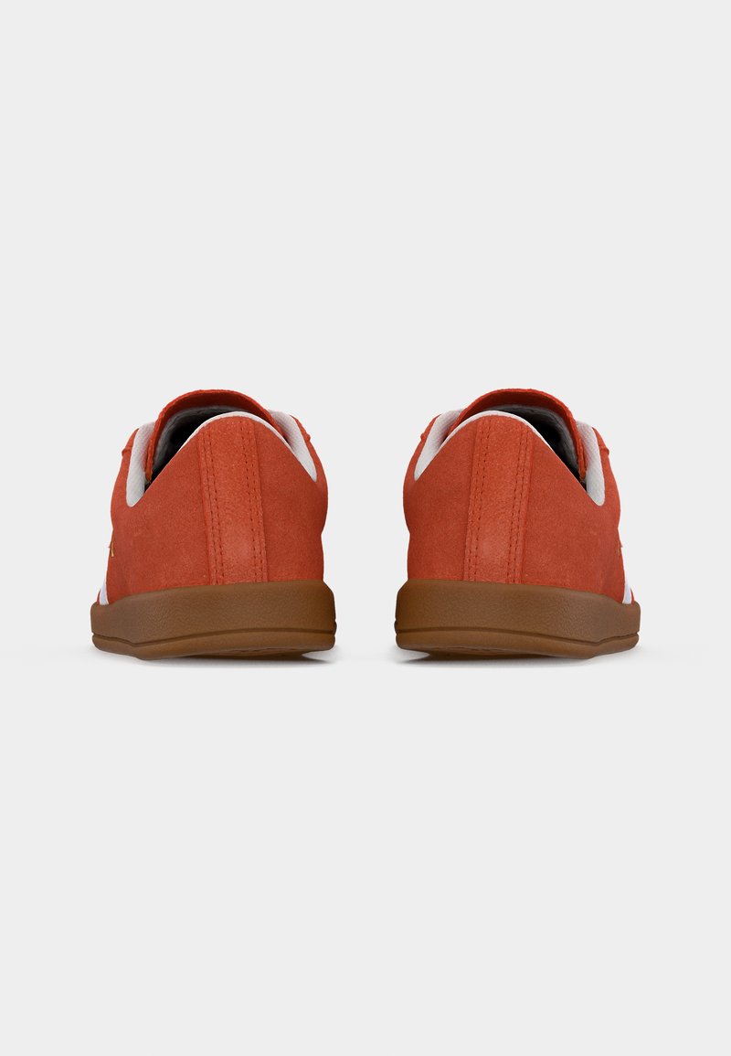 Par de zapatillas bajas de ante rojo con forro interior blanco y suelas de goma marrón, vistas desde atrás sobre un fondo blanco.