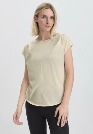 Maglietta beige a maniche corte con scollatura rotonda, texture liscia e vestibilità morbida. Abbinata a leggings neri per un look casual.