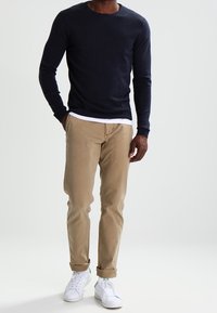 Marinblå långärmad tröja med rund hals, kombinerad med beiga chinos och vita sneakers. Outfitten har en avslappnad passform och mjuka texturer.