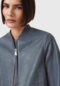 Giacca bomber in pelle grigia con una texture liscia, zip frontale e colletto a coste. Presenta tasche laterali e un design minimalista.