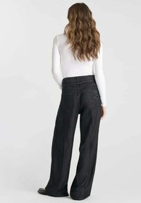 Wijdvallende zwarte denimbroek heeft een hoge taille, achterzakken en subtiele stiksels. Gecombineerd met een witte top met lange mouwen.