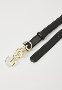 Černý kožený opasek s přezkou s designérským zlatým logem, položený na světlém pozadí, což zdůrazňuje design a texturu opasku.