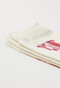Servilletas de algodón en color crema, apiladas con una textura tejida. Presentan un diseño impreso en rojo y azul en una de ellas. Bordes limpios, acabado suave.