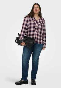 Camicia a quadri rossa, bianca e blu con volant lungo il colletto; abbinata a jeans scuri e mocassini neri. Tiene una borsa nera.
