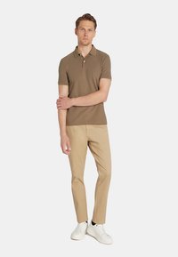 Brązowa polo z krótkim rękawem w zestawieniu z beżowymi spodniami slim-fit i białymi trampkami. Koszulka ma klasyczny kołnierzyk i subtelną teksturę.