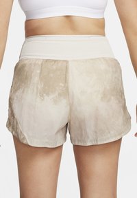 Lettvektige, beige treningsshorts med jevn tekstur, med bred elastisk midje og et subtilt tie-dye-mønster.