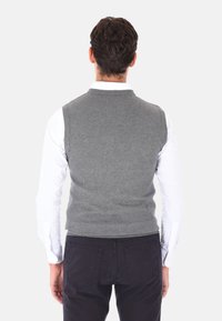 Maglione grigio senza maniche in materiale lavorato a maglia, con scollatura rotonda, abbinato a una camicia bianca a maniche lunghe e pantaloni scuri.