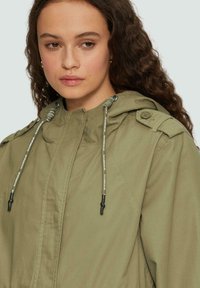 Olijfgroene jack met capuchon, voorzien van trekkoorden, een rits aan de voorkant, knoopschouderepauletten en een gestructureerde stof.