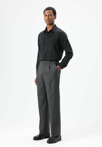 Zwart overhemd met lange mouwen en knopen, met een gladde textuur, gecombineerd met grijze geplooide pantalons en zwarte lederen schoenen.