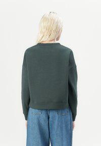 Dark green cropped sweatshirt with a round neckline and dropped shoulders, paired with light blue loose-fitting jeans. Smooth texture.