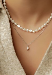 Collares en capas que presentan perlas blancas irregulares y una cadena de plata. Un collar tiene un colgante de perla en forma de lágrima. Apariencia texturizada.