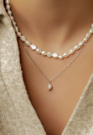 Layered necklaces featuring irregular white pearls and a silver chain. One necklace has a teardrop-shaped pearl pendant. Textured appearance.