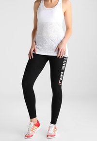 Czarne legginsy z pionowym napisem "FUTURE GIRL" w kolorze białym. Biały top na ramiączkach, czerwono-różowe buty sportowe z teksturowaną podeszwą.