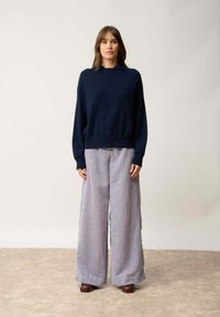 Granatowy sweter z dzianiny o wysokim kołnierzu, połączony z jasnoszarymi spodniami w paski i brązowymi butami na obcasie. Prosta, swobodna sylwetka.